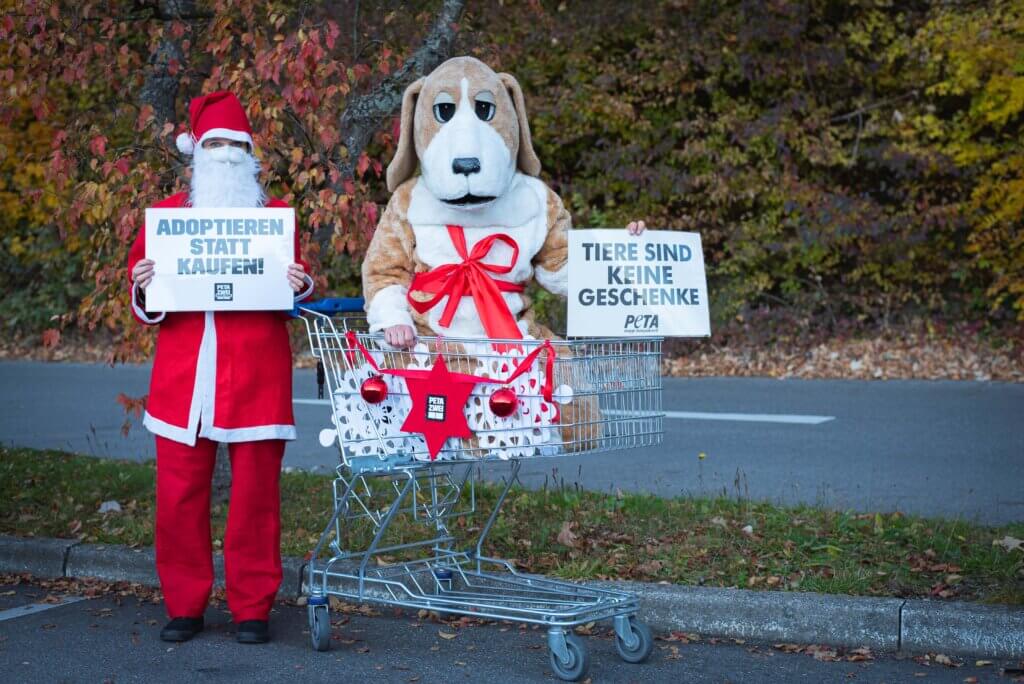Zwei Aktive in Weihnachtsmann- und Hundekostüm. Sie halten Schilder mit den Aufschriften "Adoptieren statt kaufen!" und "Tiere sind keine Geschenke".