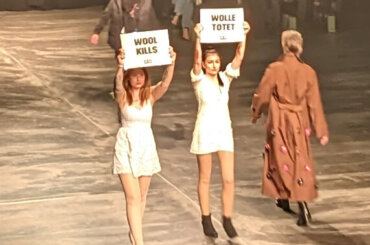Zwei Aktive auf einem Laufsteg der Fashion Week halten Schilder