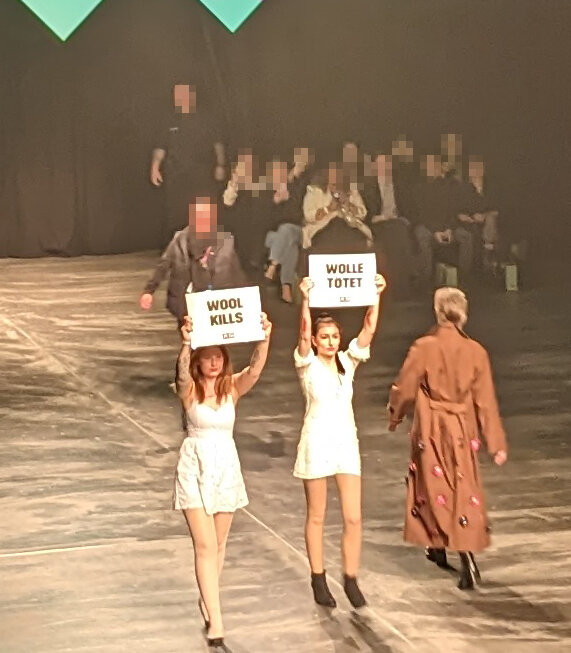 Zwei Aktive auf einem Laufsteg der Fashion Week halten Schilder