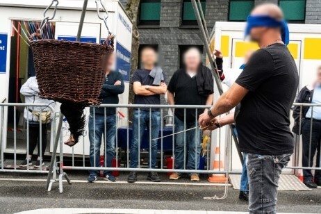 Ein Mann mit verbundenen Augen schlägt mit einem Stock nach einem über Kopf aufgehongenen Hahnenkopf