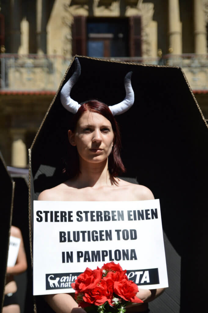 Aktive mit Stierhörnern steht in einem Sarg und hält ein Schild und Blumen 