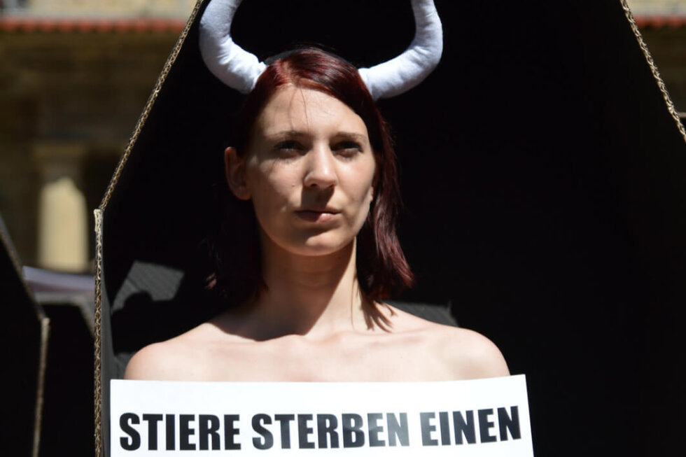 Aktive mit Stierhörnern steht in einem Sarg und hält ein Schild und Blumen