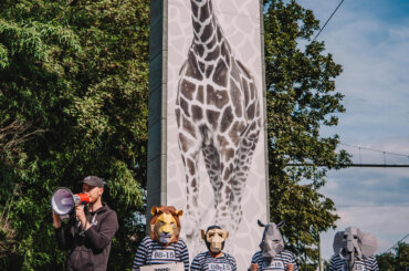 Ein Aktiver mit einem Megaphon und weitere Aktive mit Tiermasken und Sträflingskostümen stehen vor dem Eingang des Duisburger Zoos