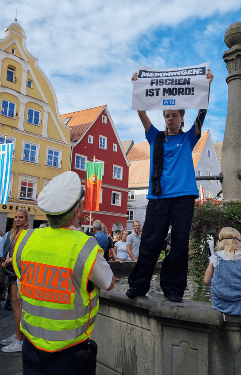 PETA-Aktivistin hält Schild hoch. Aufschrift: Fischen ist Mord!