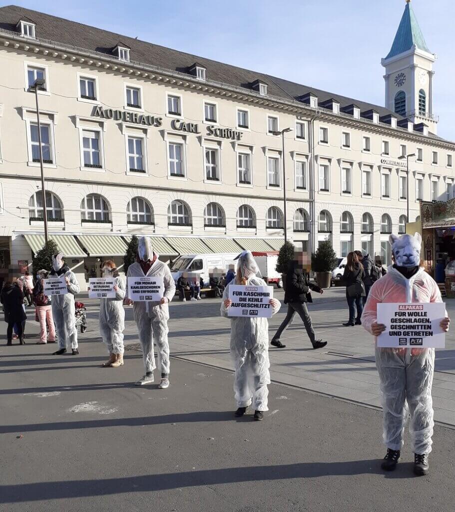 Aktive protestieren in weißen Anzügen und mit Tiermasken bekleidet gegen Wolle.