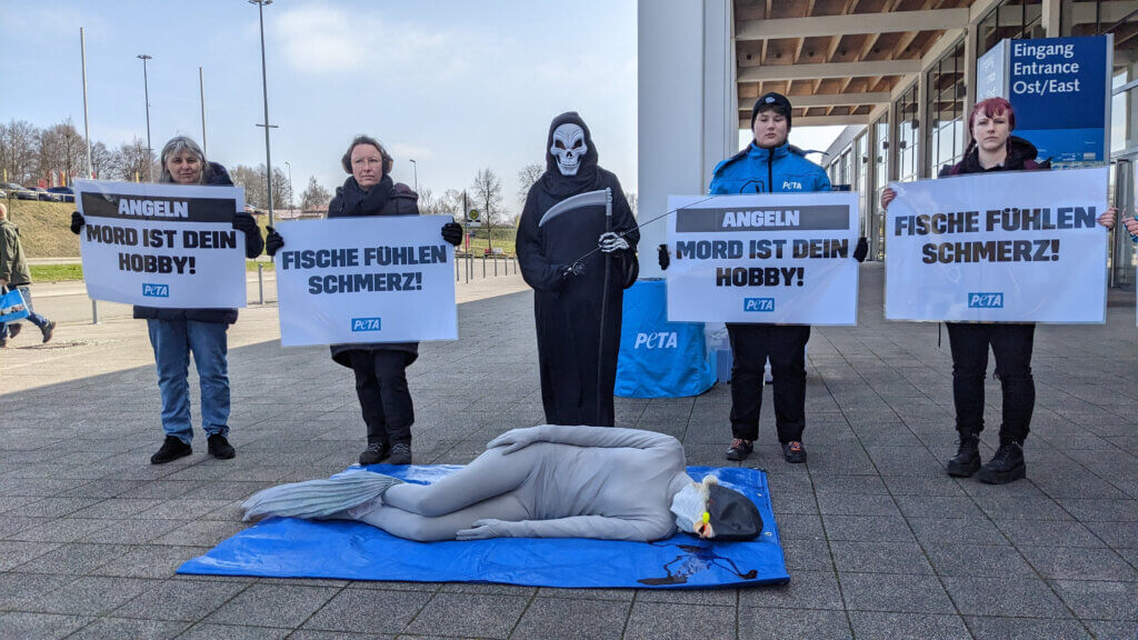 Demnonstrierende halten Schilder gegen Fischmord. Mittig ein Sensenmann, auf dem Boden ein toter "Fisch".