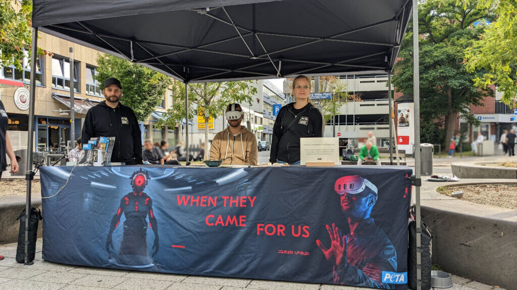 Ein Aktivist und eine Aktivistin stehen an ihrem Stand, der mit einem großen Plakat behangen ist. Darauf steht "When they came for us."