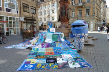 Zwei kostümierte Demonstrierende mit dem bunten Fish Empathy Quilt.