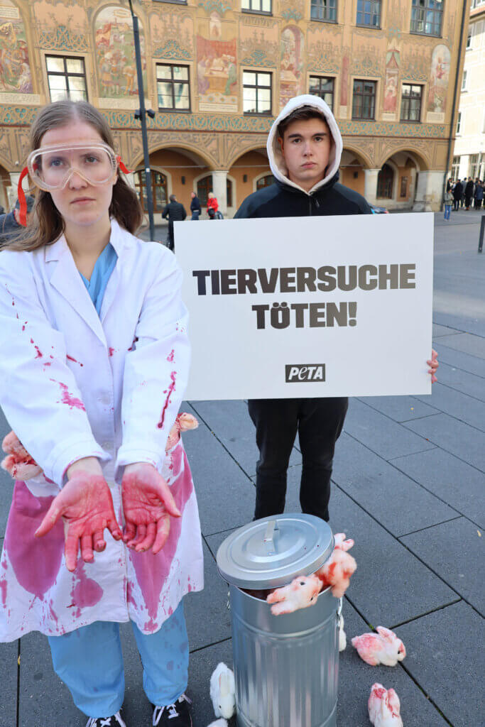 Aktive in Laborkittel mit blutigen Händen neben einem Eimer voller blutiger Plüschtiere 