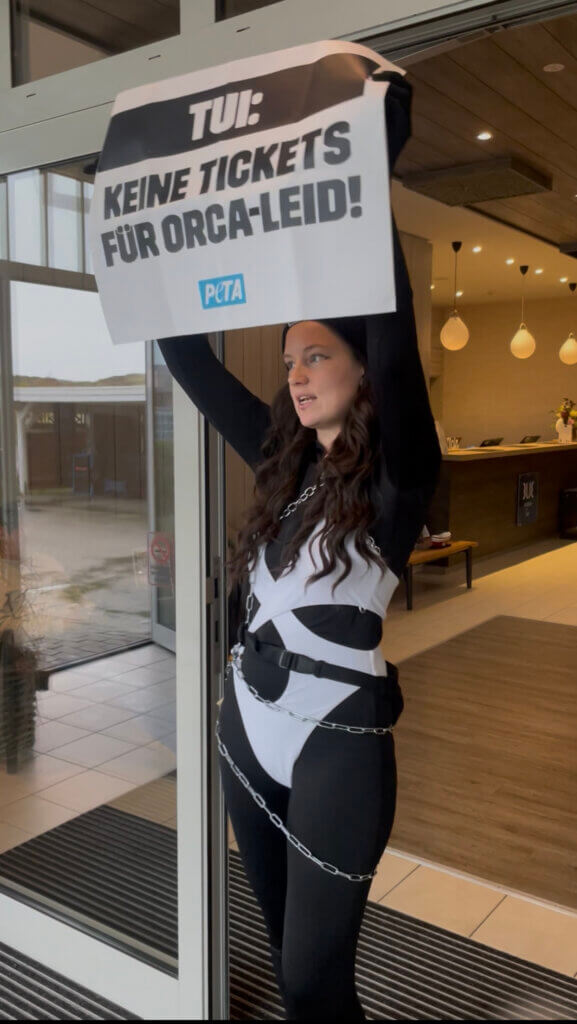Eine Frau in schwarz-weißer Kleidung hält ein Schild über ihren Kopf.