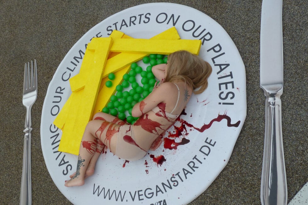 PETA-Aktion in Bonn: Eine vegane Ernährung ist konsequenter Klimaschutz. Frau liegt symbolisch auf Teller.